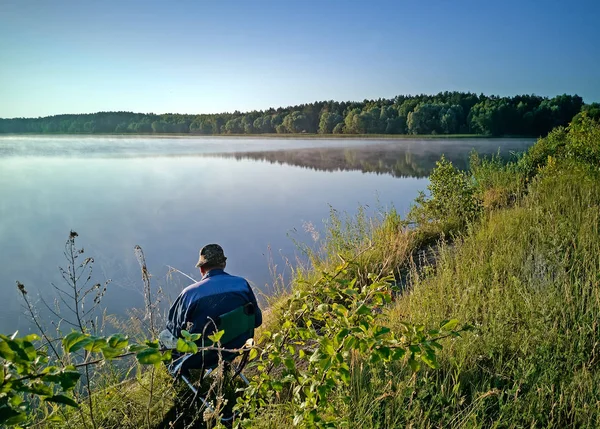 Un uomo che pesca sulla riva di un bellissimo lago . — Foto Stock