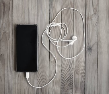 Ahşap bir arka planda akıllı telefon ve kulaklık..
