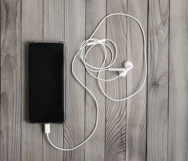 Smartphone and headphones on a wooden background.