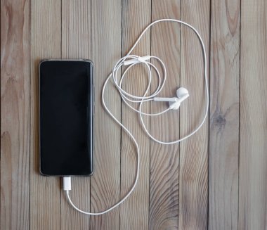 Ahşap bir masanın arka planında modern akıllı telefon ve kulaklıklar. Yakın çekim, üst görünüm, boşluğu kopyala