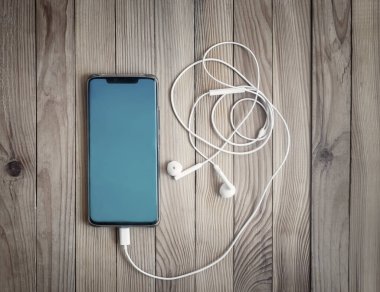 Ahşap bir masanın arka planında modern akıllı telefon ve kulaklıklar. Yakın çekim, üst görünüm, boşluğu kopyala