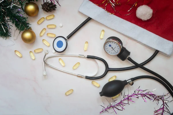 A medical poster with pills, a stethoscope, a sphygmomanometer, and Christmas decorations: garlands, toys, and a Santa Claus hat. Copy space. Christmas in medicine.