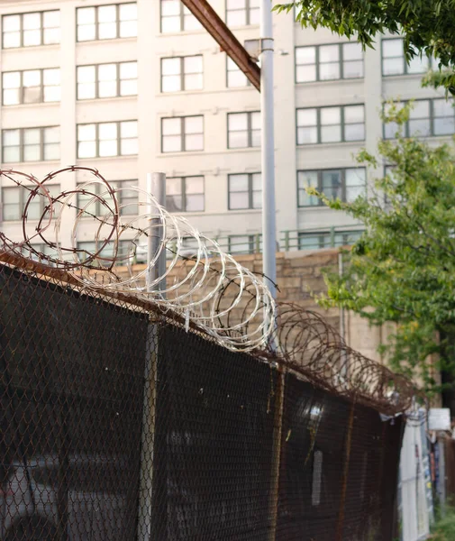Barbed wire steel wall against the brick wall and building, blurred background of trees and buildings