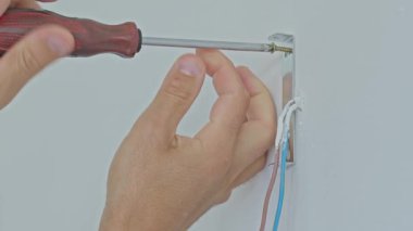 Elektrikçi, açıkta olan elektrik kablolarının yanına metal duvar desteği yerleştirmek için tornavida kullanıyor. Ev yenileme veya elektrik tesisatı kavramı