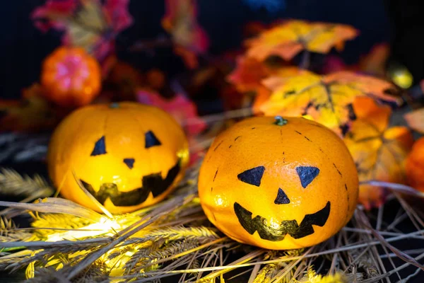 Two funny or angry pumpkins Jack Lantern head in the hay, against the background of autumn yellow leaves. One face after another on a dark wooden board, copy space