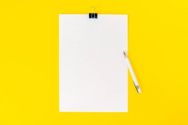 Boş bir kağıt yaprağı bir kırtasiye atacı ve sarı zemin üzerine beyaz bir kalemle bağlanır. Model, kurul duyurusu için boş bilgi, ifade, okul. Üst manzara, düz uzanma.