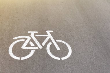 Güneşli bir günde parktaki pistte bisiklet tabelası. Simge, şehrin sokaklarındaki asfalta beyaz boya ile çizilmiş. Bisikletçi yolu, hareket yönü.