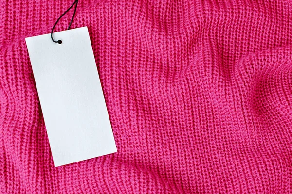 Pembe örülmüş yün kumaşların üzerinde boş fiyat etiketi var. Kasete iliştirilmiş boş bir karton bilgi kartı. Alışveriş konsepti, sonbahar ya da kış indirimi modeli, kopya alanı olan arkaplan.