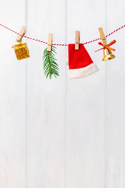 Santa Claus red hat, jingle bell, Christmas tree and gift box hangs on a rope and is attached with a wooden clothespins. Traditional symbols of the New Year on a vertically background, copy space.