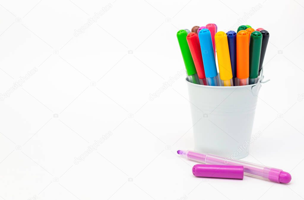 Group of multicolored markers in a white metal bucket on light background, one pen open cup, copy space. Drawing felt-tip pens, pencils, artists tools, creativity, hobby. Colorful school supplies.