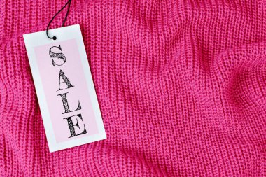 Pembe örülmüş yün kumaş, katlı ya da kazaklı kumaş üzerinde fiyat etiketi satışı. Giysilerdeki siyah banta iliştirilmiş gri desenli bir karton etiket kartı. Alışveriş kavramı, kopyalama alanı olan arkaplan.