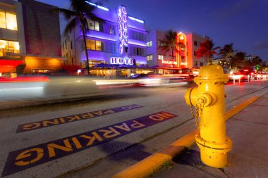 Neon ışıklar, palmiye ağaçları, arabalar ve eğlence, Miami Plajı olan insanlar ile geceleri Ocean Drive sahnesinde yangın hidrant. Ocean Drive, dünyaca ünlü destinatination üzerinde günbatımı Art Deco tarzı oteller ve restoranlar