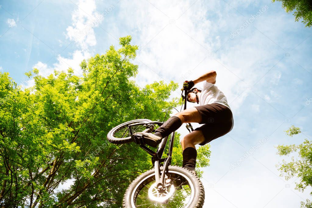 Young athlete jumping with a trial bicycle in the forest
