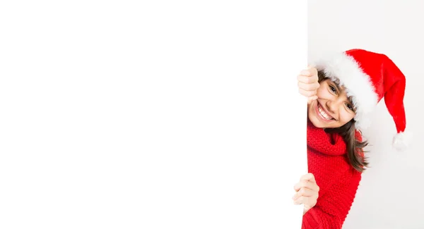可爱和滑稽的小女孩与圣诞老人帽子和红色毛衣偷看通过一个空白的广告牌 在白色上隔离 — 图库照片