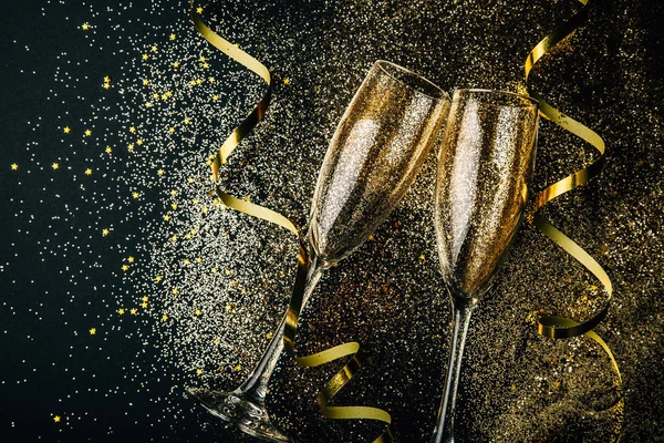 两杯香槟与金色的五彩纸屑一起烘烤 在黑暗的背景上闪闪发亮 蜿蜒曲折 庆祝的夜概念 — 图库照片