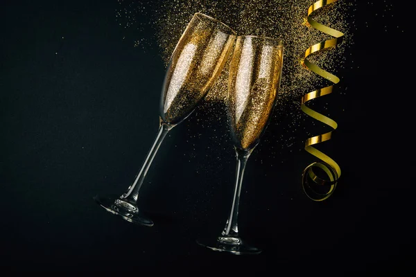 两杯香槟与金色的五彩纸屑一起烘烤 在黑暗的背景上闪闪发亮 蜿蜒曲折 庆祝的夜概念 — 图库照片
