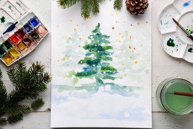 Sulu boya kutusu, fırçalar, palet ve köknar ve çam kozalakları çalışma tablosu üzerinde el yapımı suluboya Noel kartı. Üstten görünüm