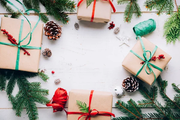 圣诞礼物与纸工艺品 拉菲亚弓 冷杉树枝别针锥和红色浆果在白色的木桌上 平面铺设 复制空间 — 图库照片