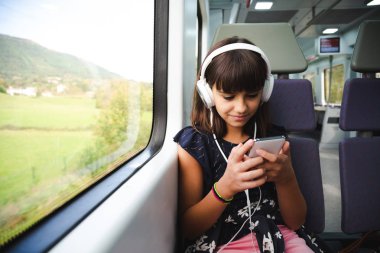 Trenle seyahat ederken onun akıllı telefon kullanarak kulaklık ile mutlu küçük kız