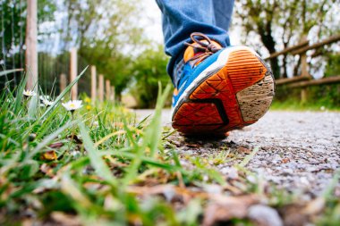 Erkek kot pantolon ve spor ayakkabı ilkbaharda bir yol boyunca yürüyüş. Ayakkabı üzerinde odaklanmak.
