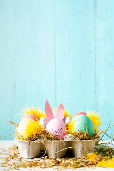 Cute and funny easter eggs with an egg decorated as a rabbit against a turquoise background, Vertical with copy space