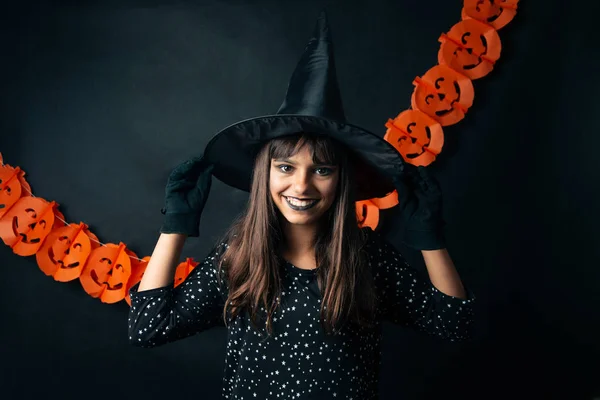 Uma Jovem Bruxa Bonita Em Um Chapéu Cônico Segura Uma Abóbora De Halloween  Em Suas Mãos E Faz Um Feitiço Com Sua Mão. Foto Royalty Free, Gravuras,  Imagens e Banco de fotografias.