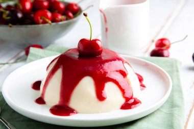 İtalyan panna cotta tatlısı, beyaz ahşap bir masada vişne soslu.