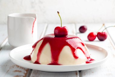 İtalyan panna cotta tatlısı, beyaz ahşap bir masada vişne soslu.
