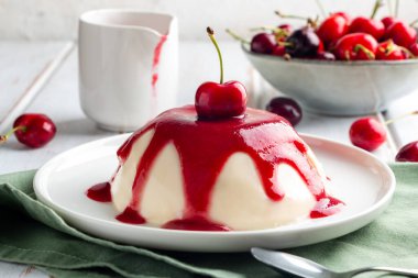 İtalyan panna cotta tatlısı, beyaz ahşap bir masada vişne soslu.