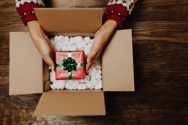 冬のセーターを詰め込んだ女性の手や素朴な木製のテーブルの上に段ボール箱からクリスマスの贈り物をアンパック クリスマスホーム配達や配送の概念 トップ表示 — ストック写真