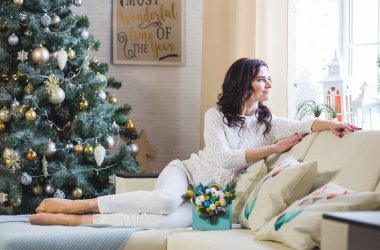 Beyaz giyen th ewhite koltukta oturan genç güzel esmer kadın pencerenin yanındaki evde kazak ördü. Noel dekorasyon ev