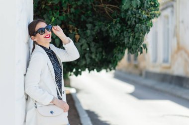 Beyaz duvar arka planda poz güneş gözlüğü trendy güzel gülen kadın Moda whilte kıyafeti.