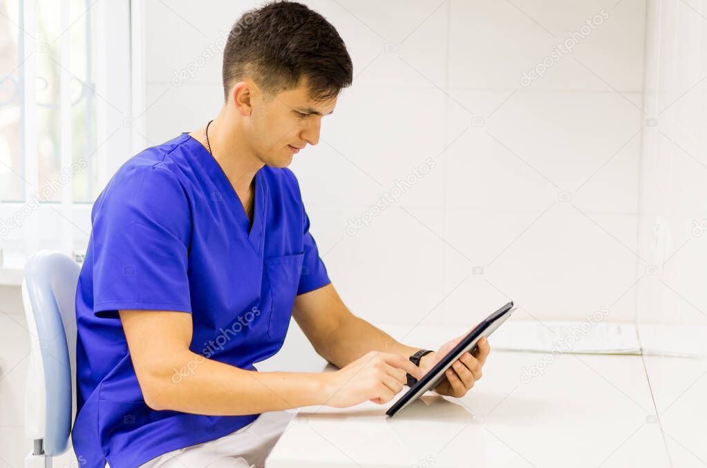 Doctor wearing blue coat working on line with a tablet in a dentist clinic.