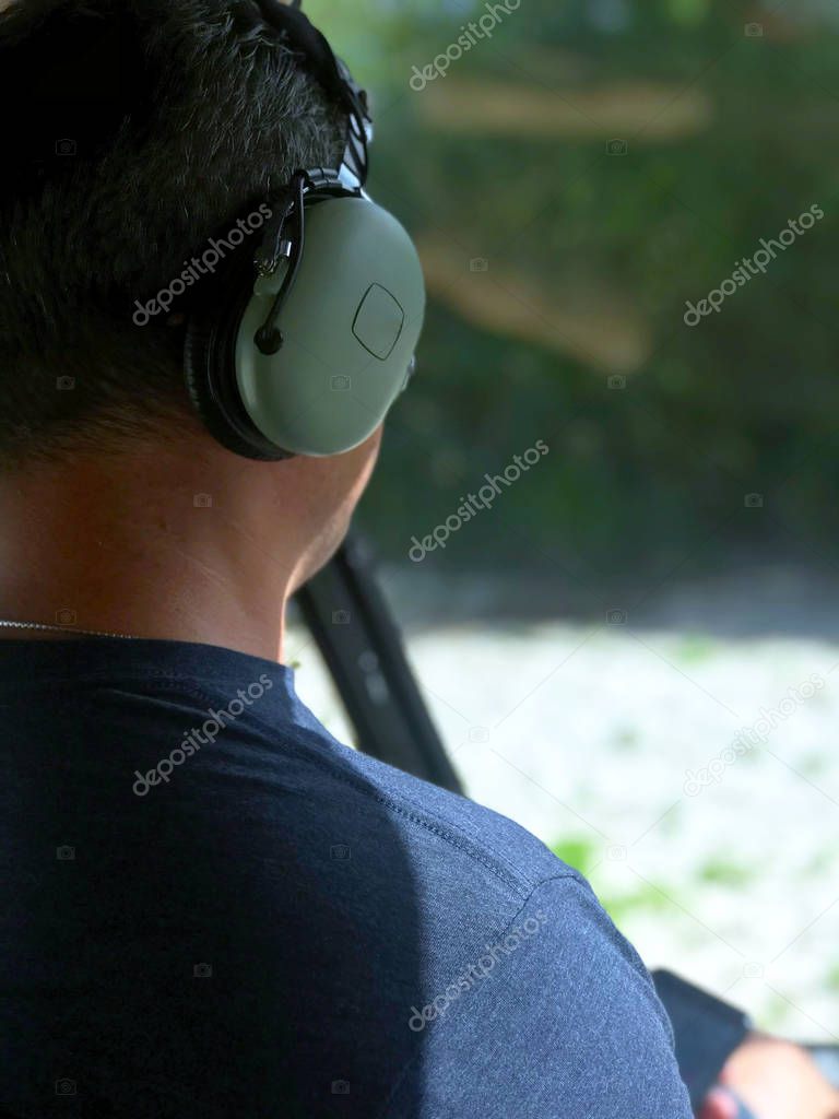 Rear view of a helicopter pilot with headphones and a remote control, which performs an excursion flight over the Caribbean Sea of the Dominican Republic and takes a photo of the sea from above