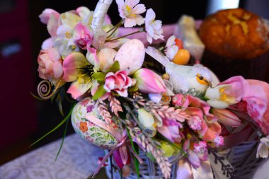 Paskalya kompozisyon. Çiçeklerle süslenmiş, boncuk, yumuşak bir beyaz tavşan yanındaki bir Paskalya sepeti bir kuş ve bir yumurta yaptı. Arka arka plan - Paskalya kek bulanık.