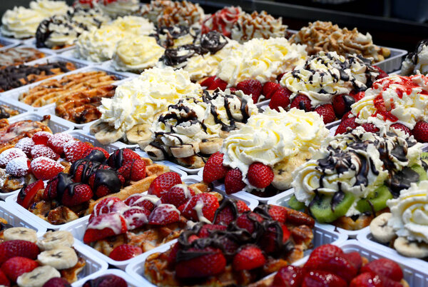 Traditional tasty, sweet and fragrant Belgian waffles with strawberries, kiwi and banana, decorated with chocolate and whipped cream on a shop window in Brussels.