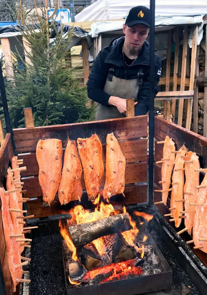 Genç bir adam plakalar ile taze somon füme bir Noel'de kömürü ve açık bir yangın bir şenlik ateşi, Brüksel'adil vardır.
