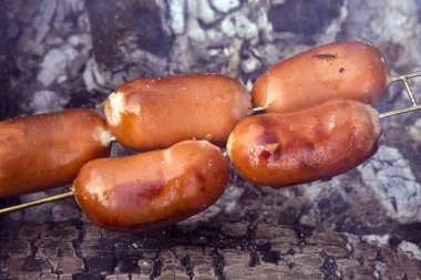 Güzel, sulu, lezzetli ve güzel kokulu kış ormandaki bir piknik kömürlerin üzerinde kavurma ızgara sosis. Etrafında duman ve aroma yükselir. Arkadaş grubu Toplantı.