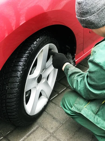 Tire fitter in green work clothes checks tire pressure. Preparing the car for a trip on the winter off-road. Maintenance.