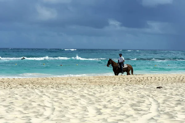 Siyah atlı Dominik polis plaj alanı devriye. Bir yağmur fırtınası önce sıcak yaz gününde Sandy beach resort Punta Cana, Dominik Cumhuriyeti.
