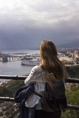 Malaga, İspanya, Şubat 2019. Yalnız bir kız bir tepe üzerinde duruyor ve sıcak güneşli bir günde Malaga İspanyolca şehir güzel panorama adlı görünüyor. Yalnız seyahat.