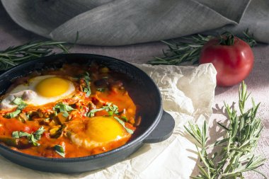 Shakshuka bir sos domates, acı biber, soğan ve baharatlar siyah bir dökme demir tava üzerinde kızarmış yumurta, lezzetli bir yemektir. Domates, pan, peçete ve parlak sabah güneş ışınlarının biberiye.