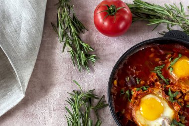 Shakshuka bir sos domates, acı biber, soğan ve baharatlar siyah bir dökme demir tava üzerinde kızarmış yumurta, lezzetli bir yemektir. Domates, pan, peçete ve parlak sabah güneş ışınlarının biberiye.