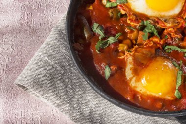 Shakshuka bir sos domates, acı biber, soğan ve baharatlar siyah bir dökme demir tava üzerinde kızarmış yumurta, lezzetli bir yemektir. Domates, pan, peçete ve parlak sabah güneş ışınlarının biberiye.