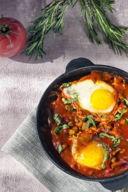 Shakshuka bir sos domates, acı biber, soğan ve baharatlar siyah bir dökme demir tava üzerinde kızarmış yumurta, lezzetli bir yemektir. Domates, pan, peçete ve parlak sabah güneş ışınlarının biberiye.