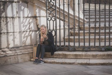 Malaga, İspanya, Şubat 2019. Genç bir kız ünlü Malagan Enkarnasyon Katedrali'nin mermer merdivenlerinde oturur ve dondurma yer. Malaga Katedrali şehrin cazibe olduğunu. Yolculukta mola.