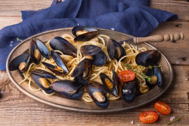 Midyeile spagetti, eski ahşap masanın üzerinde orijinal tabakta baharatlı soslu domates. İstiridye Mytilus yakın çekim. İtalyan makarnası. Romantik bir akşam yemeği için bir tabak.