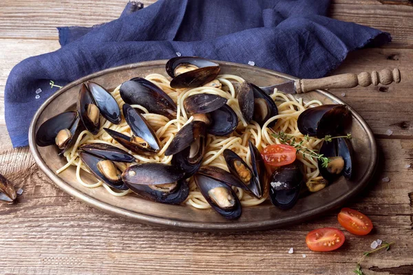 Midyeile spagetti, eski ahşap masanın üzerinde orijinal tabakta baharatlı soslu domates. İstiridye Mytilus yakın çekim. İtalyan makarnası. Romantik bir akşam yemeği için bir tabak.