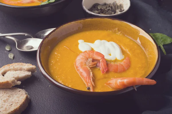 2 dishes of orange pumpkin soup on a black table. Three red shrimps decorate the soup. Spinach, pumpkin seeds and croutons lie on the table. Delicious dinner. Beautiful presentation of dishes. — Stock Image 2 dishes of orange pumpkin soup on a black table. Three red shrimps decorate the soup. Spinach, pumpkin seeds and croutons lie on the table. Delicious dinner. Beautiful presentation of dishes. Royalty Free Stock Photos