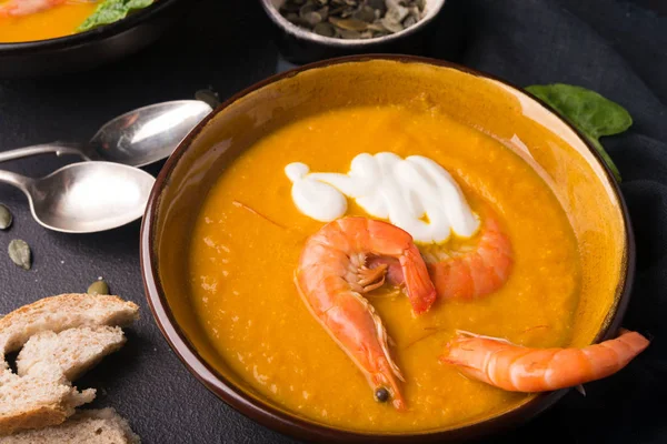 2 dishes of orange pumpkin soup on a black table. Three red shrimps decorate the soup. Spinach, pumpkin seeds and croutons lie on the table. Delicious dinner. Beautiful presentation of dishes. — Stock Image 2 dishes of orange pumpkin soup on a black table. Three red shrimps decorate the soup. Spinach, pumpkin seeds and croutons lie on the table. Delicious dinner. Beautiful presentation of dishes. Royalty Free Stock Images